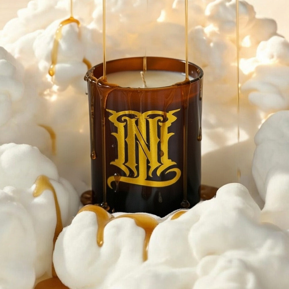 Candle with gold logo in a decorative setting with white clouds and lights