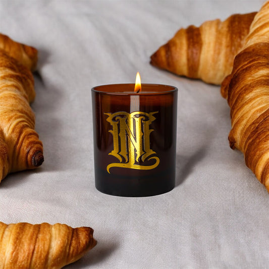 Candle with gold emblem surrounded by croissants on a light background
