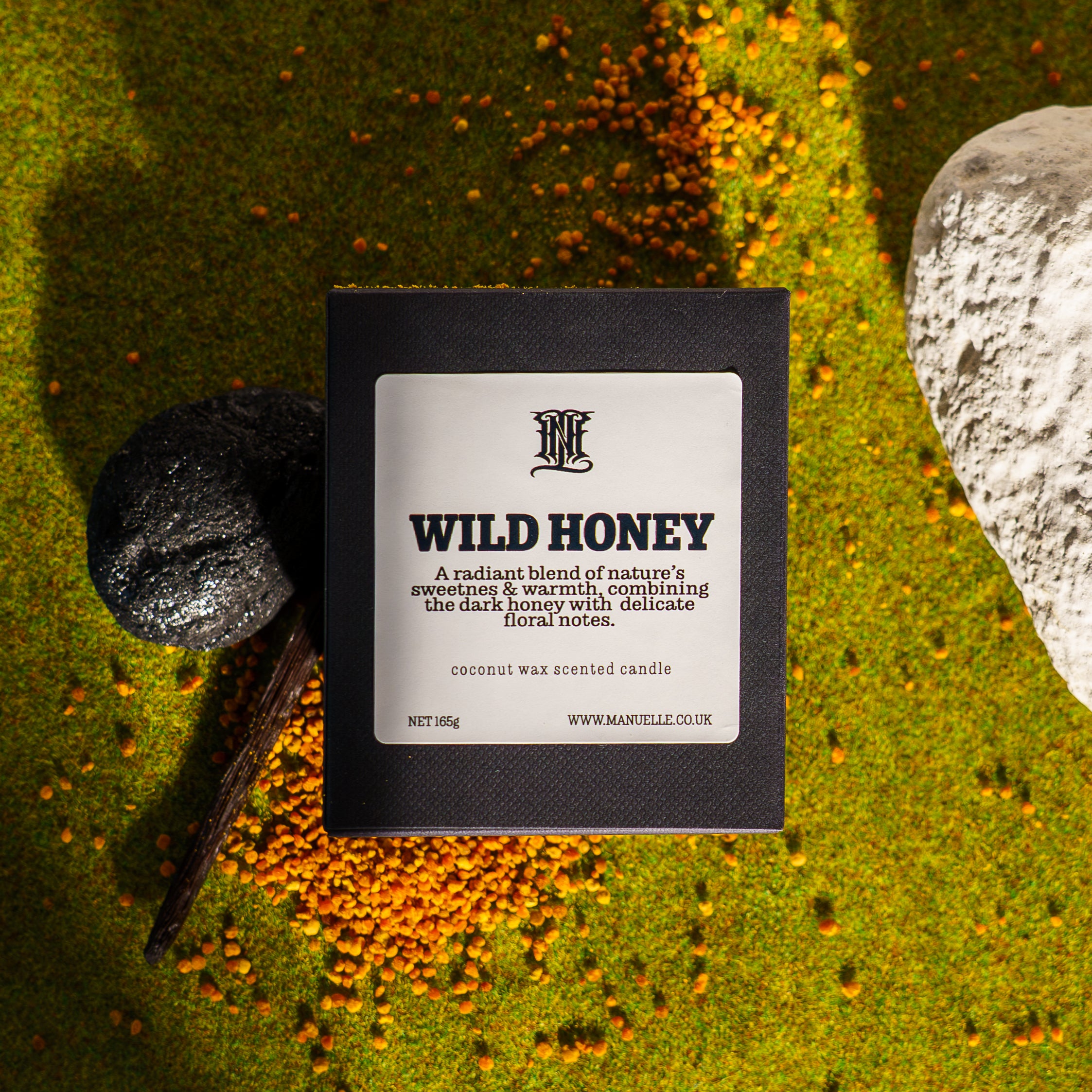 Manuelle candle labeled 'Wild Honey' on a natural background with stones and foliage.