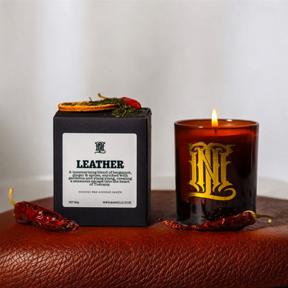 Candle labeled 'Leather' with packaging on a textured surface