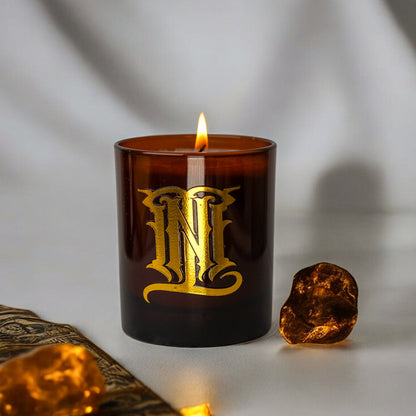 Candle in a brown glass container with gold lettering on a neutral background