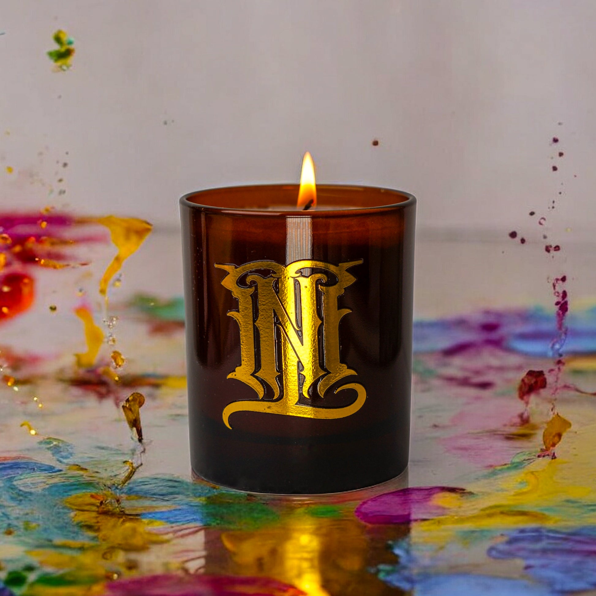 Candle with gold lettering on a colorful abstract background