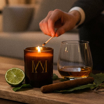 Candle being lit with a match, surrounded by a glass of whiskey, lime, and cinnamon on a wooden surface.