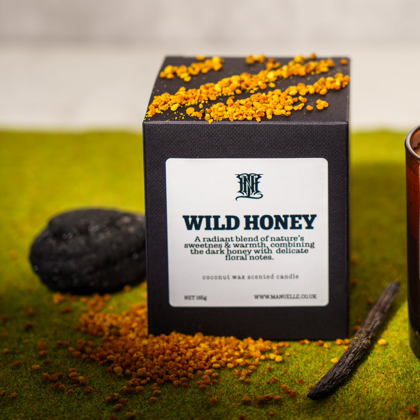 Black candle box labeled 'Wild Honey' with decorative elements on a green surface.