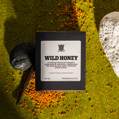 Manuelle candle labeled 'Wild Honey' on a natural background with stones and foliage.