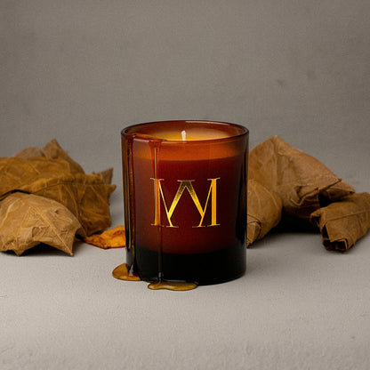 Candle with a gold 'M' logo on a gray background